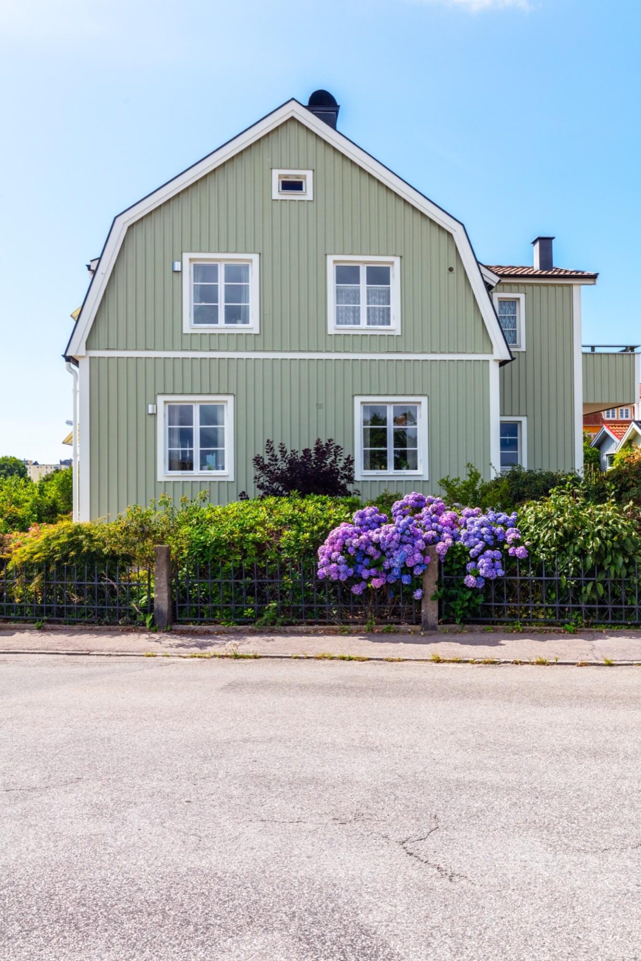 Ett grönmålat boende med elegant vit fasadutsmyckning, omringat av en trädgård där lila hortensior frodas